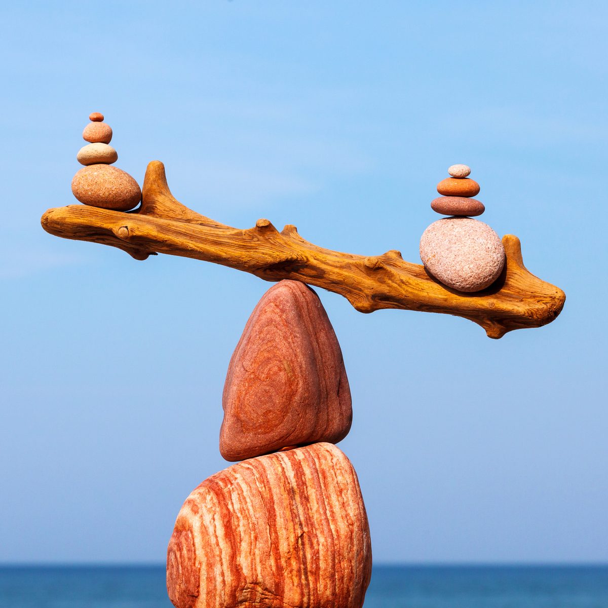 Stacked stones balanced on a length of driftwood above a calm sea