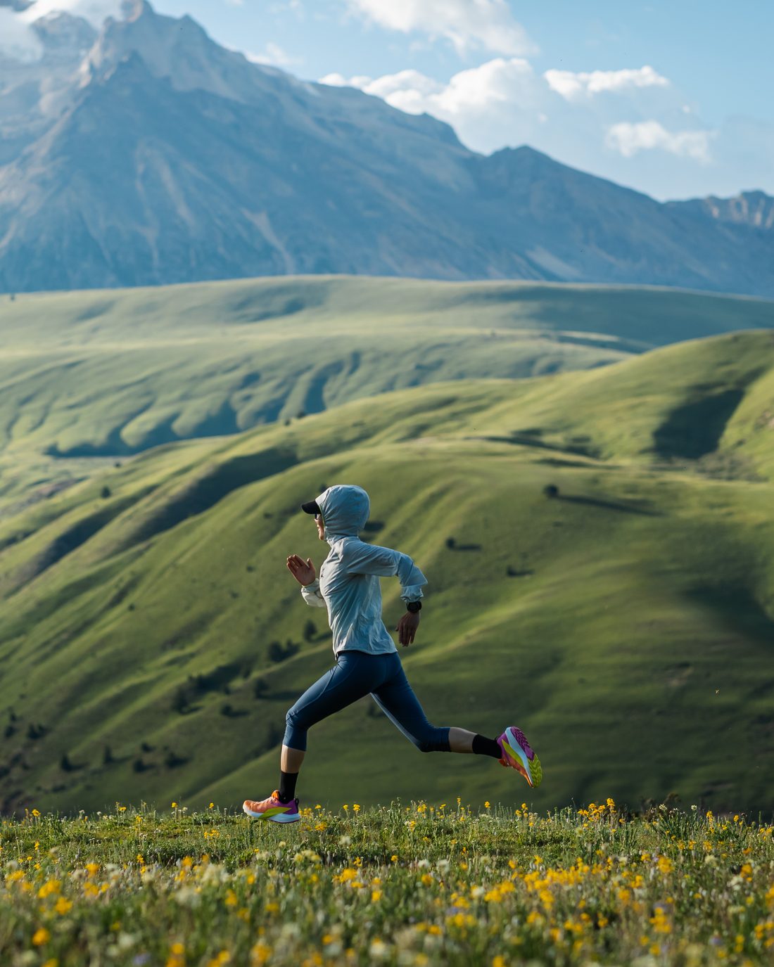 A runner crossing a high alpine meadow below snow-capped peaks